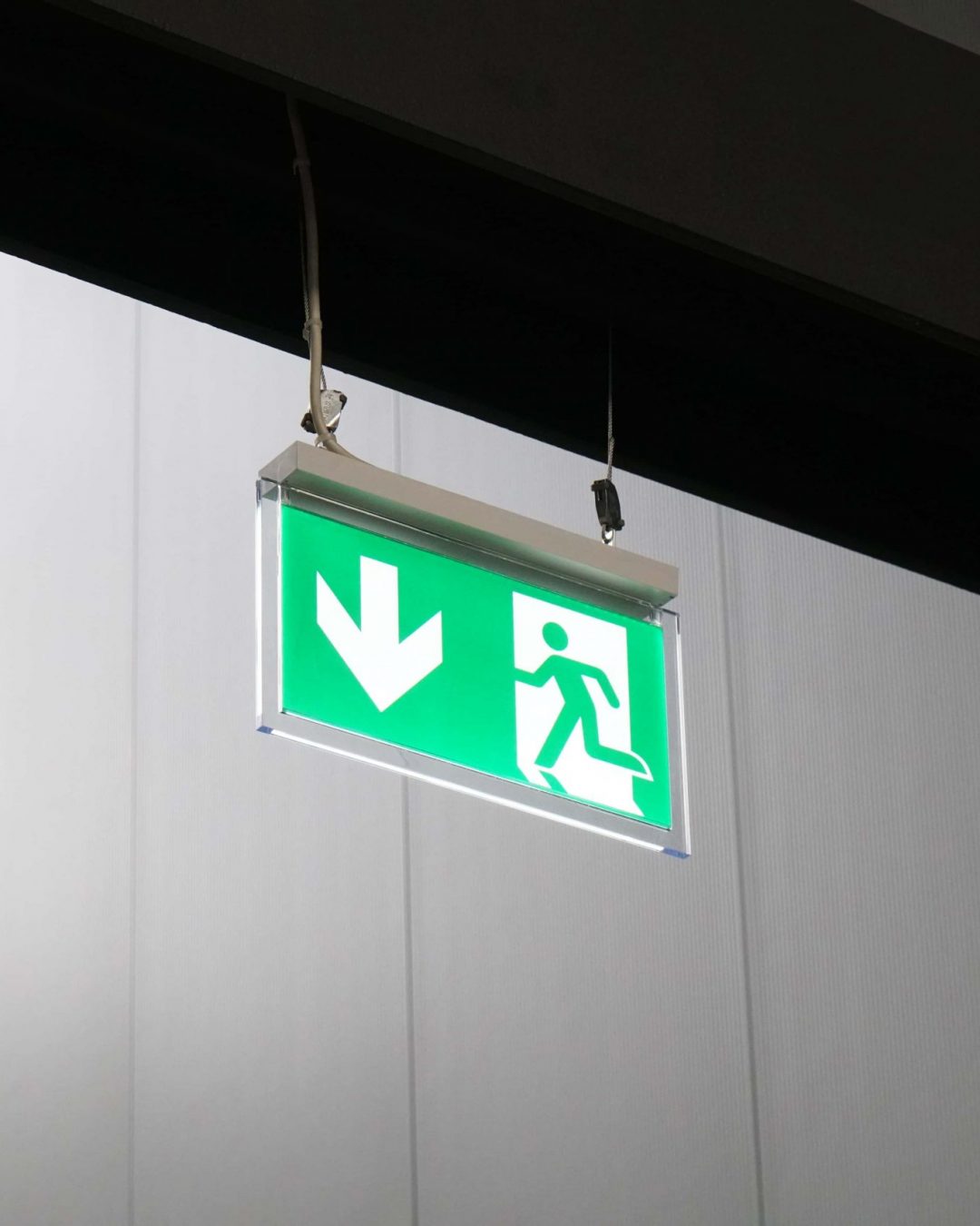 emergency exit or fire escape sign with green running man symbol and directional arrow hanging from ceiling